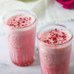 A refreshing glass of Rose Cardamom Lassi garnished with rose petals and cardamom seeds.