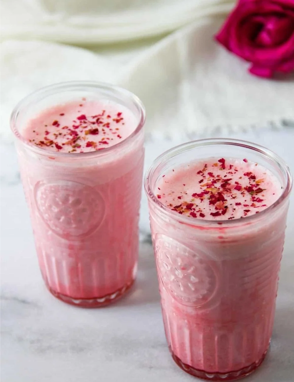 A refreshing glass of Rose Cardamom Lassi garnished with rose petals and cardamom seeds.
